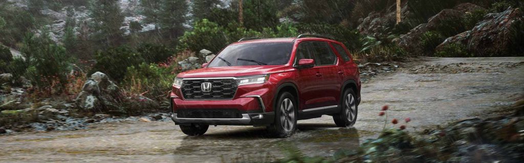A red Honda SUV driving on a wet, rocky road through a forest during a heavy downpour.